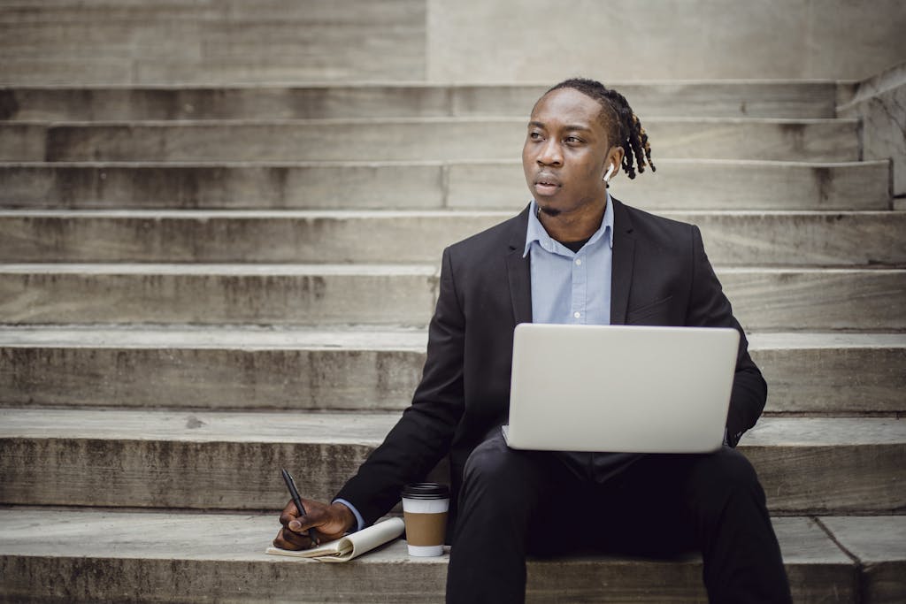 Focused young professional working on a laptop outdoors, sitting on steps.