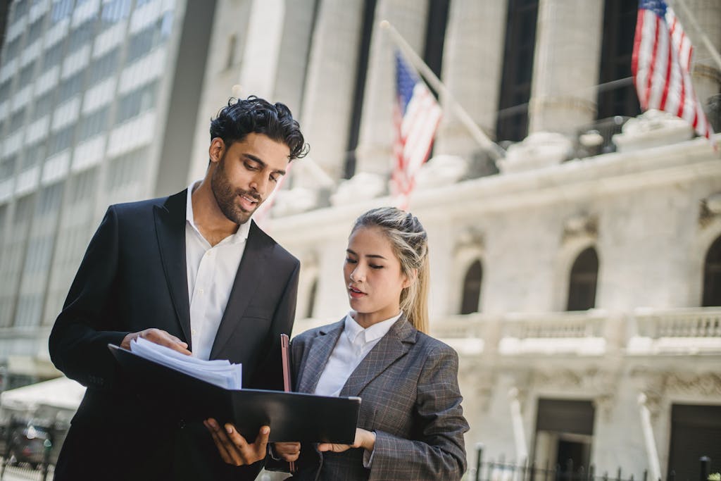 Two business professionals review documents outside a financial institution, indicating teamwork and collaboration.
