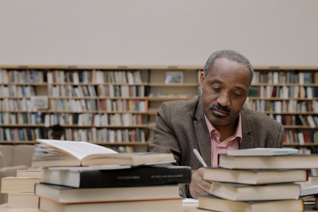 Man sits and studies with books in a library, emphasizing focus and learning.